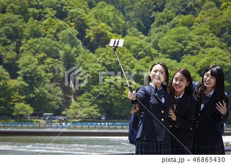 川を背景に自撮り棒で自撮りする二人の女子高生の写真素材