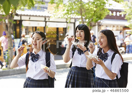 団子を食べながら通りを歩く三人の女子高生 46865500