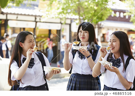 団子を食べながら通りを歩く三人の女子高生の写真素材