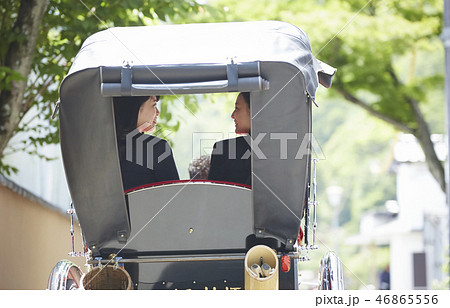 通りを行く人力車に乗る二人の女子高生の背中の写真素材