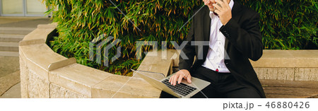 Manager talking by smartphone and working with laptop outside in 46880426