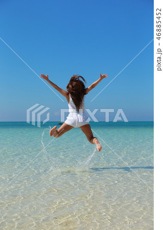綺麗な海でジャンプする女性の後ろ姿の写真素材