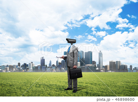 Camera headed man standing on green grass against modern cityscape 46898600