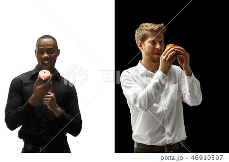 Men eating a hamburger and donut on a black and white background Men eating a hamburger and donut on a black and white background 46910397