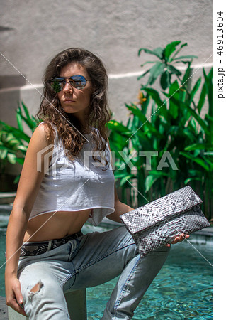 Woman hands with snakeskin python luxury bag near the swimming pool. belt and clutch made of natural Woman hands with snakeskin python luxury bag near the swimming pool. belt and clutch made of natural 46913604