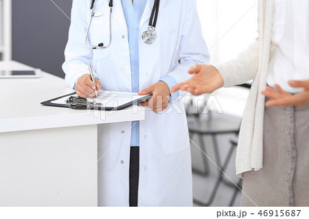 Unknown doctor and  female patient  discussing something while standing near reception desk 46915687