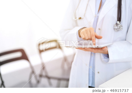 Female physician using digital tablet  while standing near reception desk at clinic or emergenc 46915737
