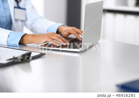 Unknown doctor woman typing on laptop computer while sitting at the desk in hospital office. close Unknown doctor woman typing on laptop computer while sitting at the desk in hospital office. close 46916285