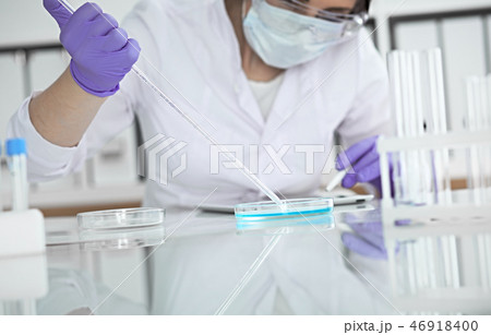 Close-up of professional female scientist in protective eyeglasses making experiment with reagents Close-up of professional female scientist in protective eyeglasses making experiment with reagents 46918400