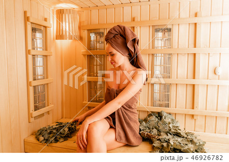 Young woman relaxing in a sauna dressed in a towel. Interior of new Finnish sauna, infrared panels 46926782