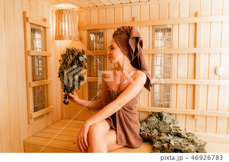 Young woman relaxing in a sauna dressed in a towel. Interior of new Finnish sauna, infrared panels 46926783