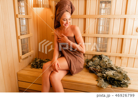Young woman relaxing in a sauna dressed in a towel. Interior of new Finnish sauna, infrared panels Young woman relaxing in a sauna dressed in a towel. Interior of new Finnish sauna, infrared panels 46926799