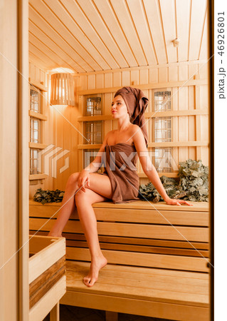 Young woman relaxing in a sauna dressed in a towel. Interior of new Finnish sauna, infrared panels Young woman relaxing in a sauna dressed in a towel. Interior of new Finnish sauna, infrared panels 46926801