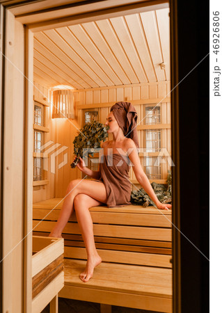 Young woman relaxing in a sauna dressed in a towel. Interior of new Finnish sauna, infrared panels 46926806