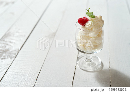 Glass of dessert with whipped cream with a fresh mint leaf and raspberry on white table. 46948091