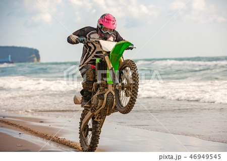 Motorcyclist in a protective suit rides a motorcycle on the sea, splashes fly from under the wheels. 46949545