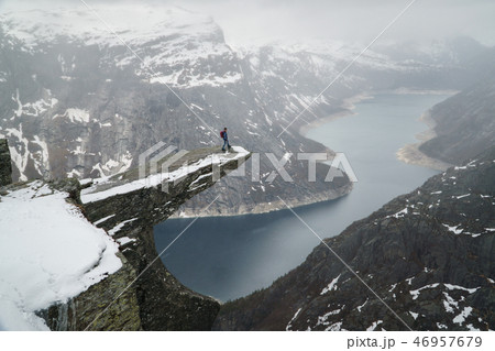 Trolltunga cliff under snow in Norway. Scenic Landscape. Man traveller standing on edge of rock and Trolltunga cliff under snow in Norway. Scenic Landscape. Man traveller standing on edge of rock and 46957679