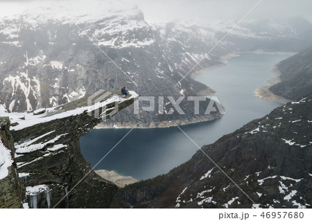 Trolltunga cliff under snow in Norway. Scenic Landscape. Man traveller sitting on edge of rock in Trolltunga cliff under snow in Norway. Scenic Landscape. Man traveller sitting on edge of rock in 46957680