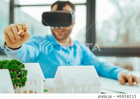Happy man holding a pencil and pointing to a miniature house 46958215
