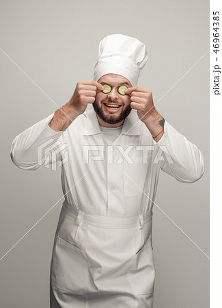 Cheerful cook holding cucumber slices near eyes Cheerful cook holding cucumber slices near eyes 46964385