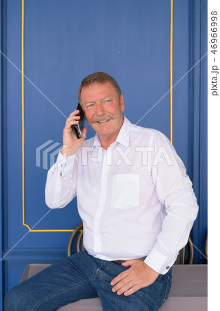 Happy senior businessman thinking while talking on the phone against blue wall Happy senior businessman thinking while talking on the phone against blue wall 46966998