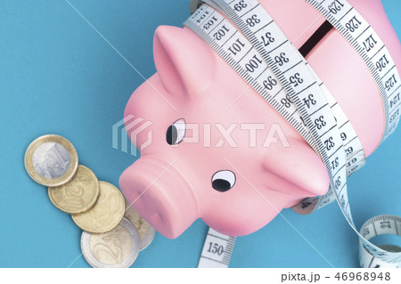 Investments and metering or counting idea. Ceramic toy pig with white flexible ruler on blue Investments and metering or counting idea. Ceramic toy pig with white flexible ruler on blue 46968948