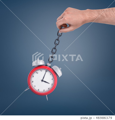 A large male hand holding a metal chain with a red retro clock swinging on it. 46986379