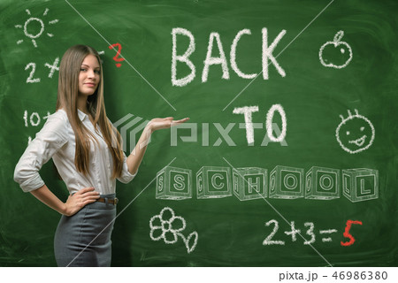 A beautiful businesswoman or a teacher standing half-turn on a school board background pointing at A beautiful businesswoman or a teacher standing half-turn on a school board background pointing at 46986380