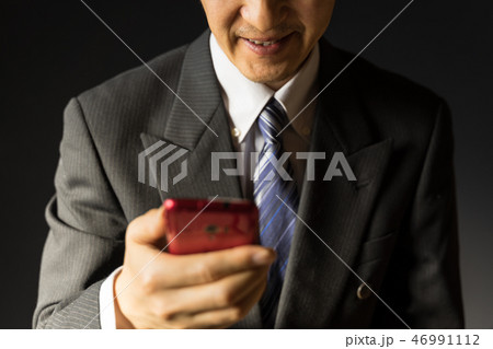 スマホを見ながら薄笑いを浮かべる無精髭のビジネスマン スマホを見ながら薄笑いを浮かべる無精髭のビジネスマン 46991112