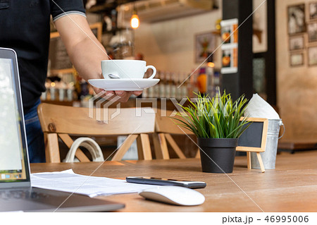 Male waiter serving coffee with laptop and glasses on working table in cafe. Male waiter serving coffee with laptop and glasses on working table in cafe. 46995006