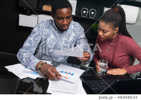 two young black people discuss their business using diagrams sitting at Desk in the office 46998634