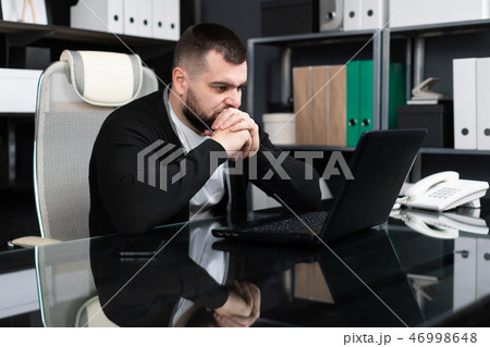 Portrait of young man sitting at table in office Portrait of young man sitting at table in office 46998648