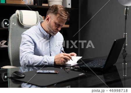 young man sitting at computer table and makes notes in diary young man sitting at computer table and makes notes in diary 46998718