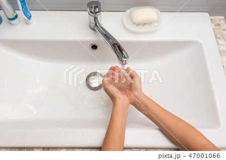 The child collects water in her hands from the mixer, top view 47001066