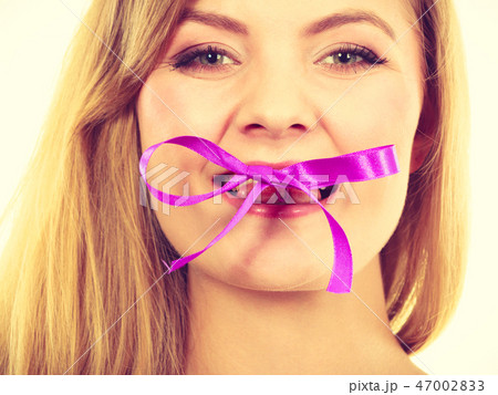 Blonde woman biting decorative purple bow 47002833