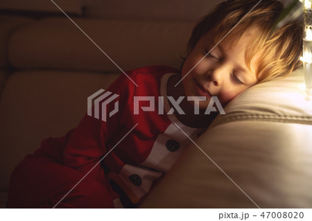 Beautiful boy sleeps on the sofa in Christmas night. Child sleeping under a Christmas tree Beautiful boy sleeps on the sofa in Christmas night. Child sleeping under a Christmas tree 47008020