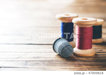 Wooden reel with thread and fingertip close-up. Wooden reel with thread and fingertip close-up. 47009818