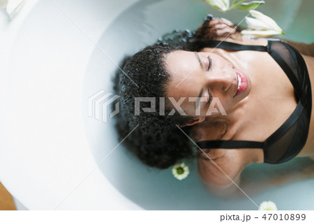 Young relaxed afro american girl taking bath and wearing black underwear, blue water background. 47010899