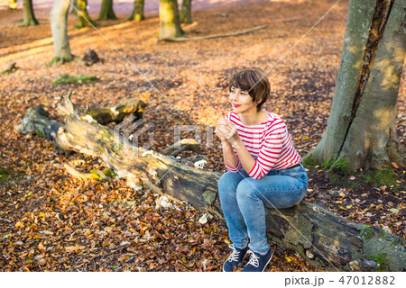 Portrait of young woman sitting on the fallen tree Portrait of young woman sitting on the fallen tree 47012882