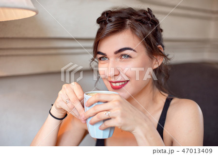 Young attractive girl in a black T-shirt and jeans sits in a cafe at the table and drinks coffee in Young attractive girl in a black T-shirt and jeans sits in a cafe at the table and drinks coffee in 47013409