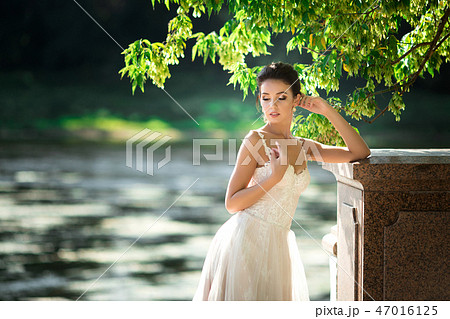 fashion photo of beautiful woman with dark hair in luxurious wedding dress posing outdoor. fashion photo of beautiful woman with dark hair in luxurious wedding dress posing outdoor. 47016125