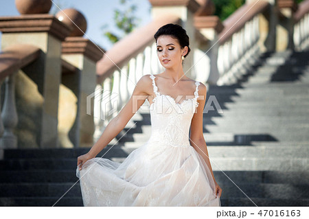fashion photo of beautiful woman with dark hair in luxurious wedding dress posing outdoor. 47016163