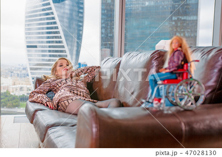 A beautiful young blonde girl in a fashionable dress with a disability, posing on a leather sofa A beautiful young blonde girl in a fashionable dress with a disability, posing on a leather sofa 47028130