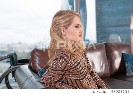 A beautiful young blonde girl in a fashionable dress with a disability, posing on a leather sofa A beautiful young blonde girl in a fashionable dress with a disability, posing on a leather sofa 47028152