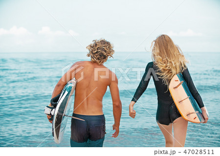 Surfers at the beach- Smiling couple of surfers walking on the beach and having fun in summer 47028511