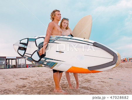 Surfers at the beach- Smiling couple of surfers walking on the beach and having fun in summer Surfers at the beach- Smiling couple of surfers walking on the beach and having fun in summer 47028682