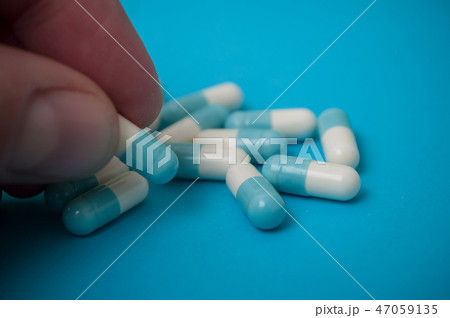 blue capsules in finger on blue background 47059135