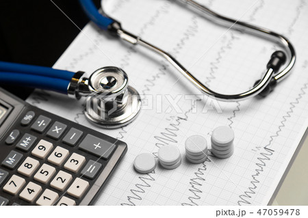 Stethoscope, pills and calculator are on a sheet with an electrocardiogram 47059478