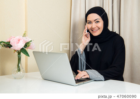 Muslim female talking on the phone while working with laptop computer. Muslim female talking on the phone while working with laptop computer. 47060090