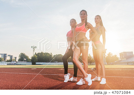 Group of fit young sportswomen standing in athletics stadium and posing. Group of fit young sportswomen standing in athletics stadium and posing. 47071084